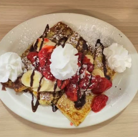 Banana split crepes with strawberries, banana, whipped cream and chocolate drizzle